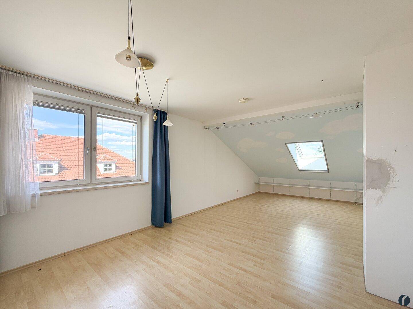 Helles Dachzimmer mit Laminatboden, Dachschrägen und großem Fenster.