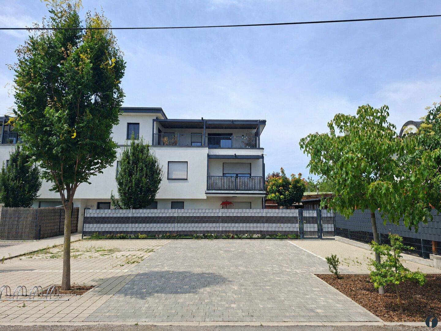 Modernes Mehrfamilienhaus mit weißer Fassade, Balkonen und gepflasterten Parkplätzen davor.