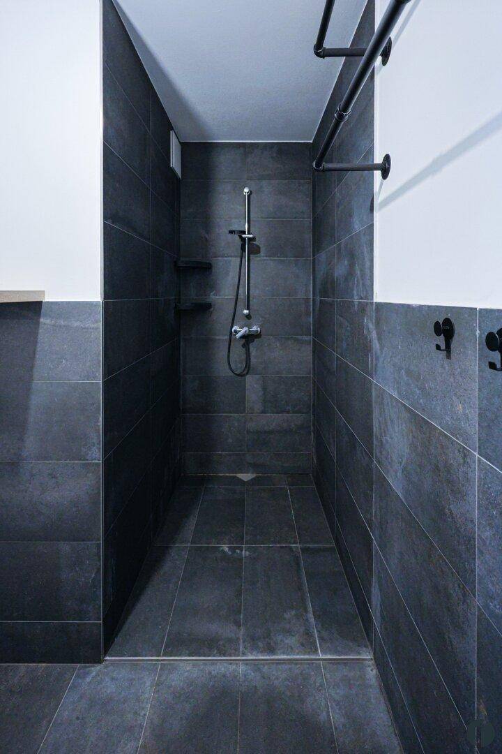 Moderne, begehbare Dusche mit dunklen Fliesen an Wänden und Boden.