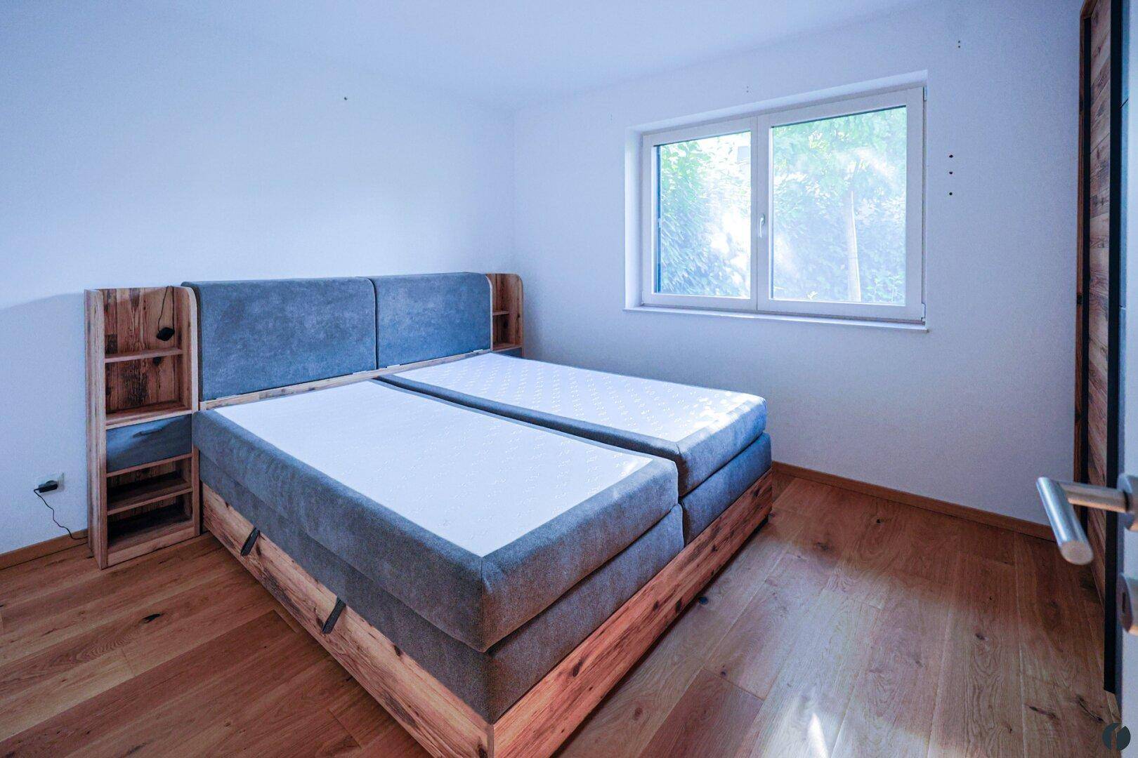 Schlafzimmer mit Holzboden und einem modernen Doppelbett mit integrierten Nachttischen.