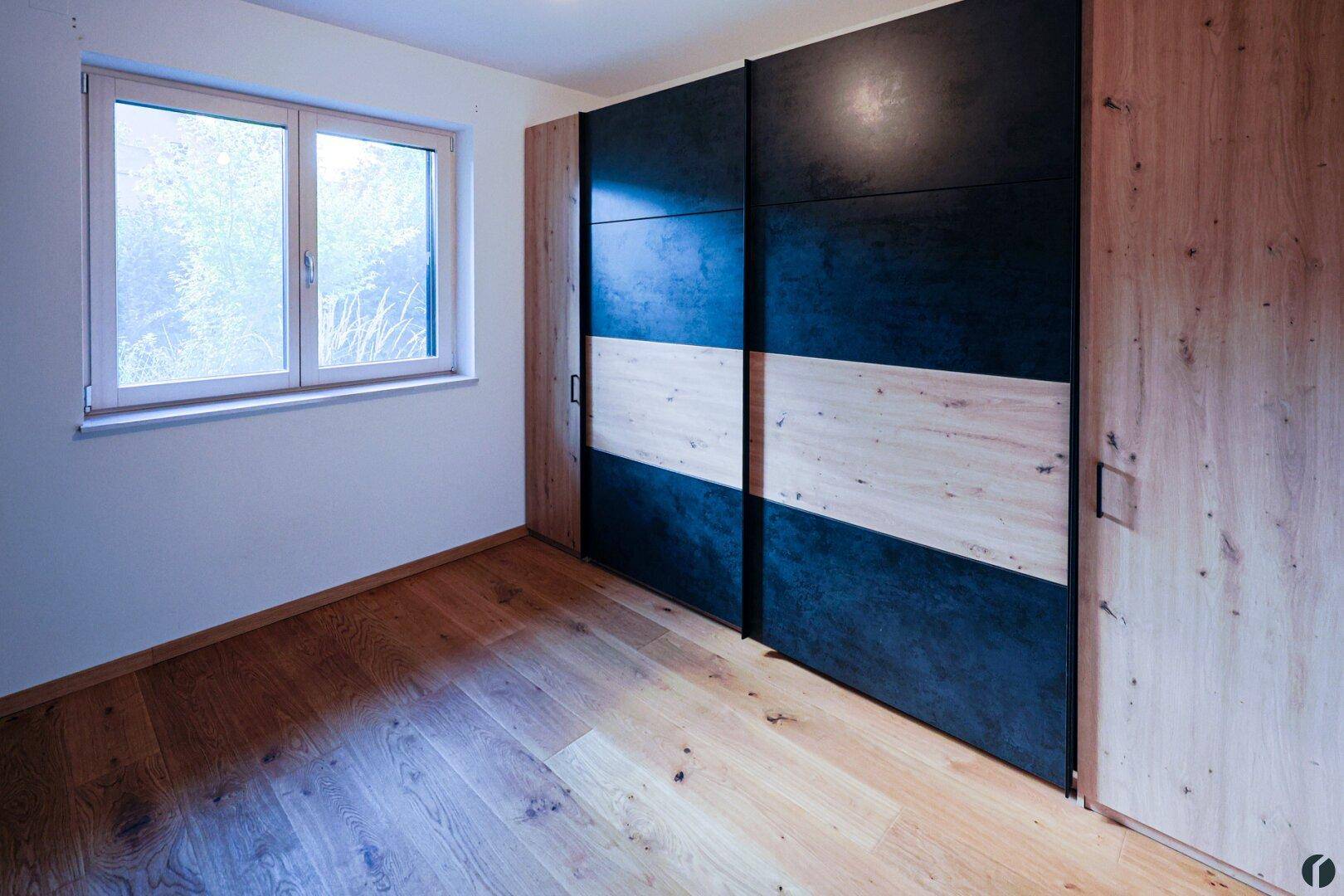 Schlafzimmer mit Holzboden und einem großen Schiebetürenschrank in Holz- und Dunkelgrau-Optik.