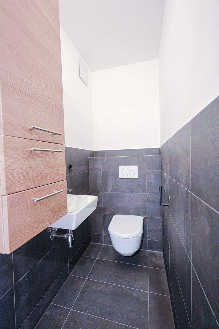 Modernes Gäste-WC mit wandhängendem WC, Waschbecken und dunklen Fliesen.