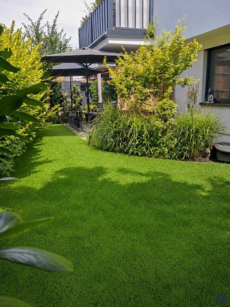 Gepflegter Garten mit Rasenfläche, Sträuchern und einer gemütlichen Sitzgelegenheit im Freien.