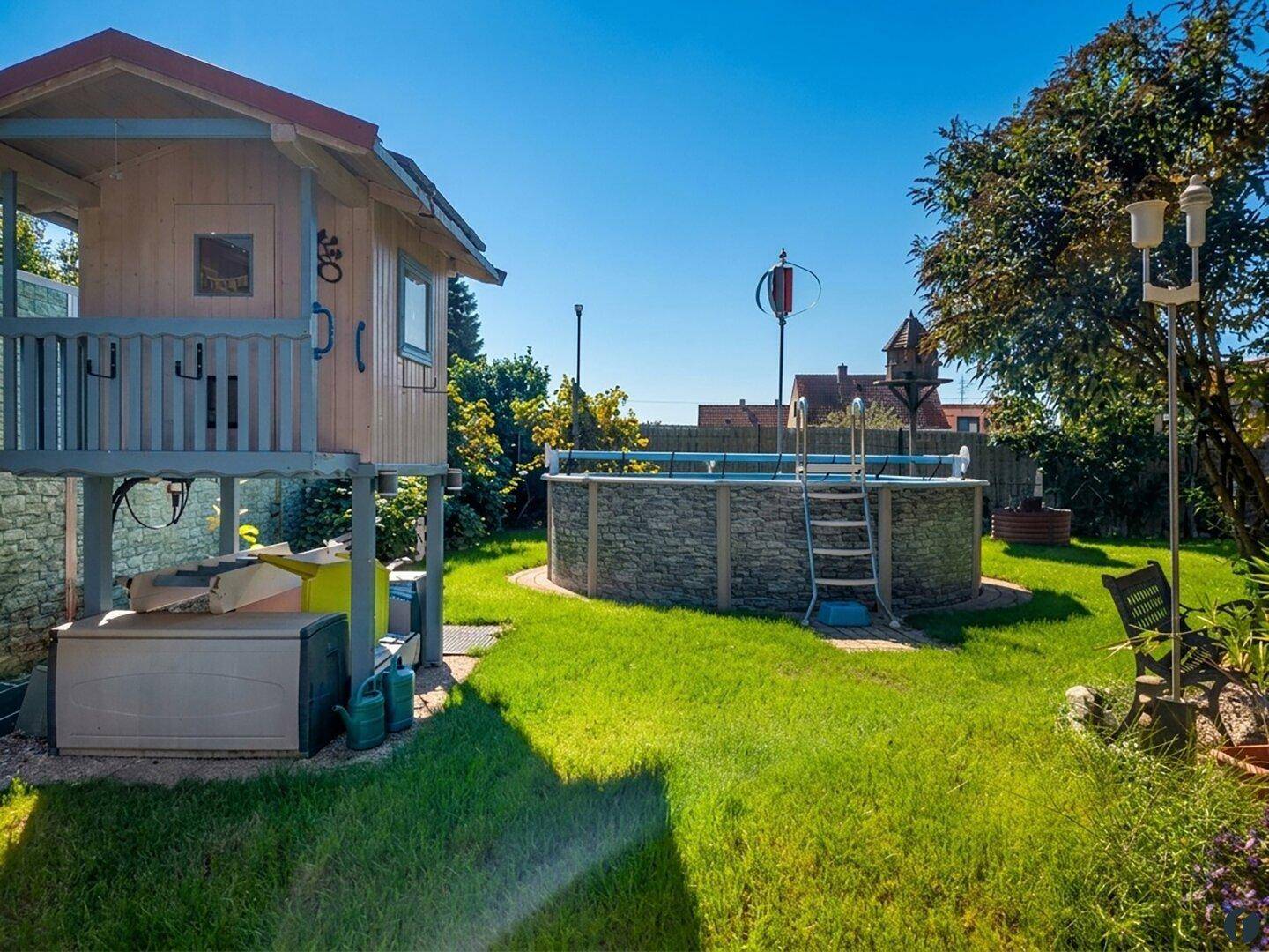 Gepflegter Gartenbereich mit Aufstellpool, Spielhaus und Rasenfläche.