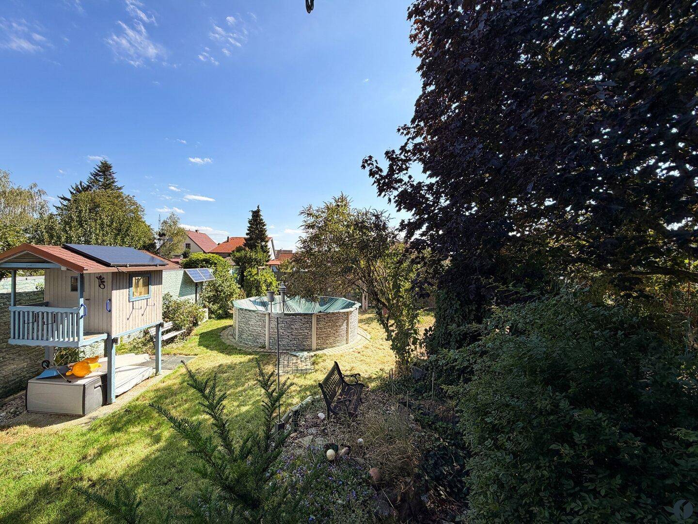 Großer Garten mit Aufstellpool, Spielhaus und viel Grünfläche.