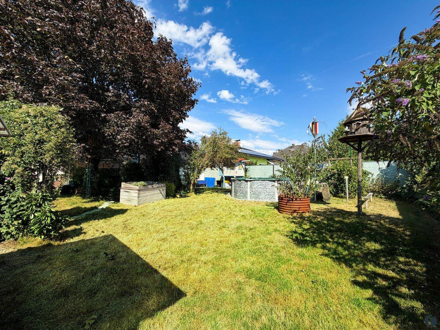 Weitläufiger Garten mit Rasenfläche, Bäumen und Blick auf die Umgebung.