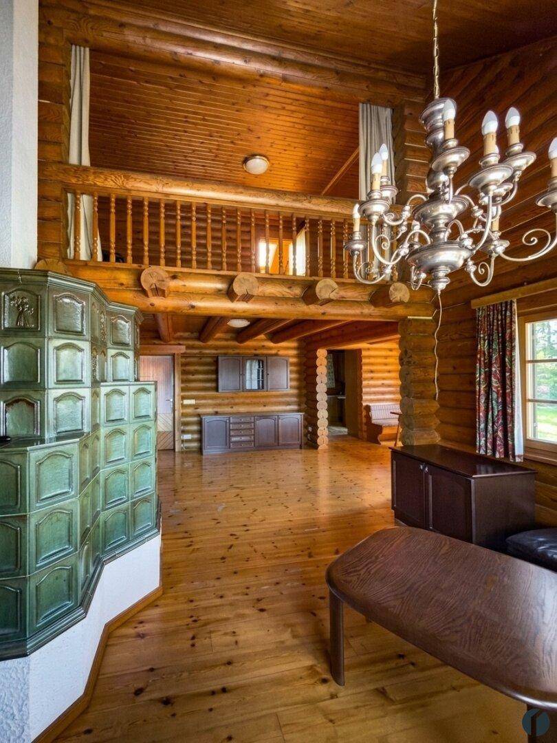 Geräumiges Wohnzimmer im Blockhausstil mit Kachelofen, Holzbalken und offener Galerie.