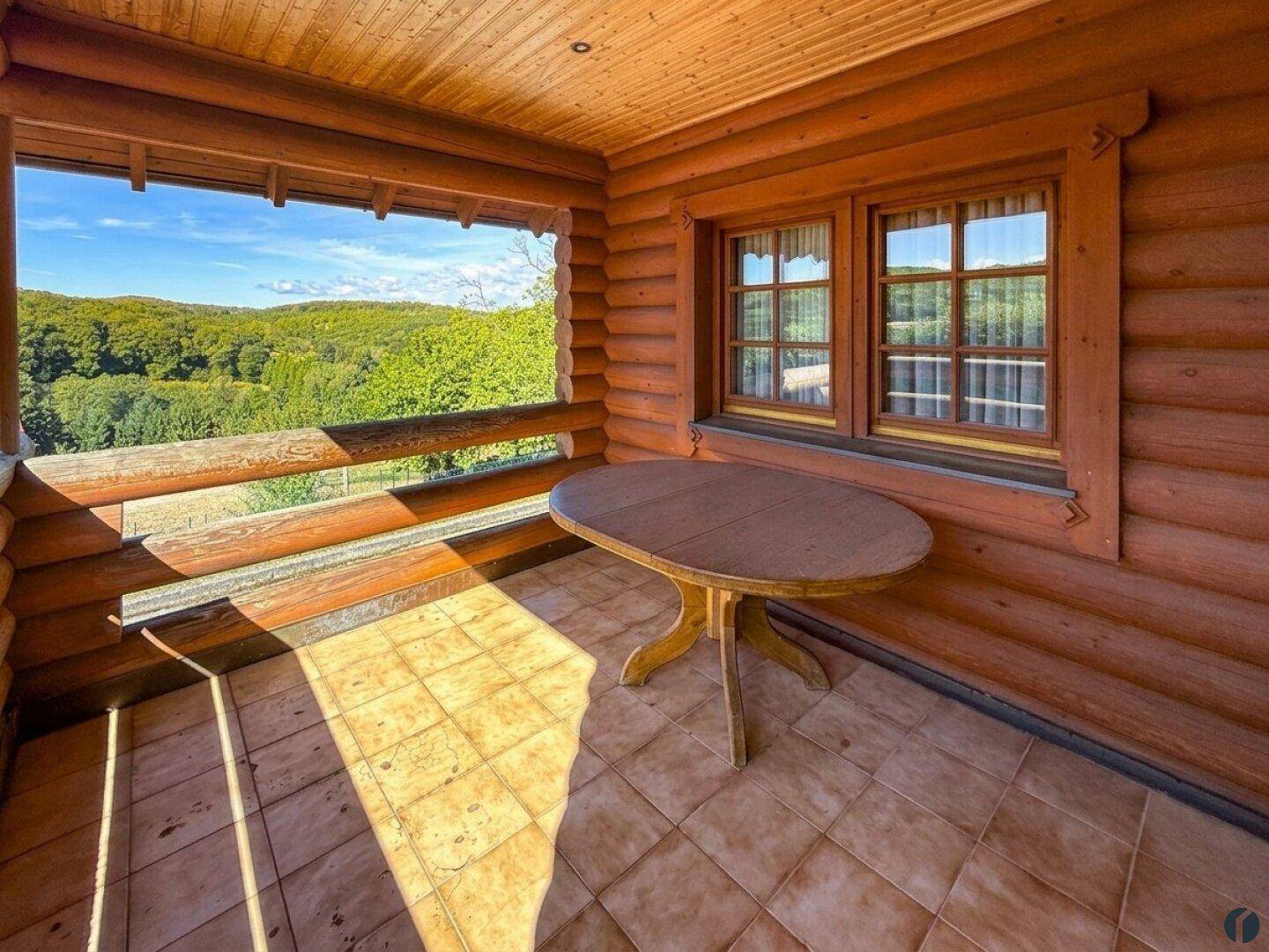 Sonniger Balkon mit Holztisch und Fliesenboden, bietet einen weiten Blick ins Grüne.
