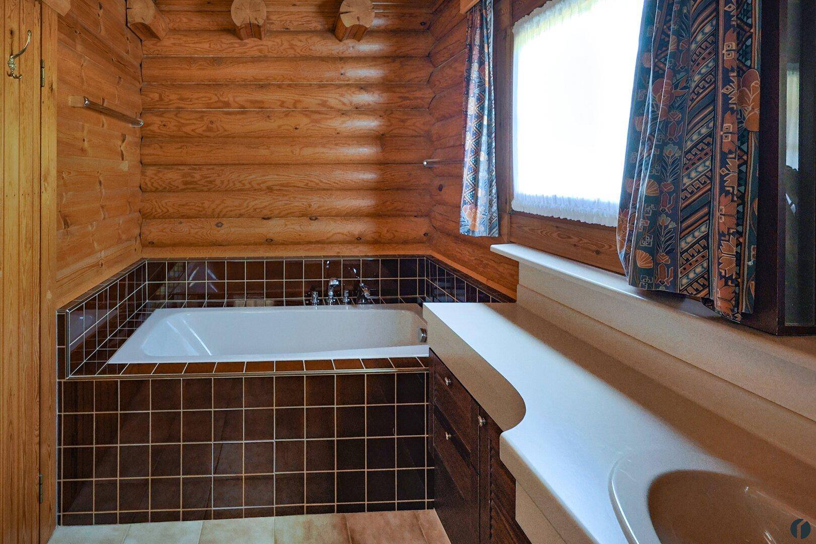 Badezimmer mit eingebauter Badewanne, braunen Fliesen und Holzverkleidung im Blockhaus.