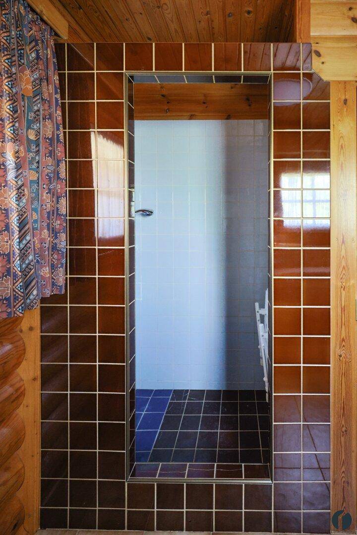 Duschbereich im Badezimmer mit braunen und weißen Fliesen, umgeben von Holzverkleidung.