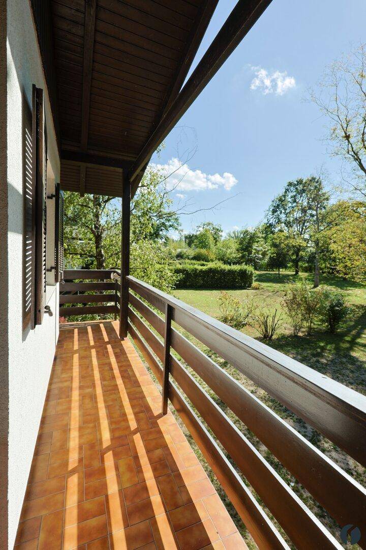 Sonniger Balkon mit Terrakottafliesen und Holzgeländer, der einen weiten Blick ins Grüne bietet.