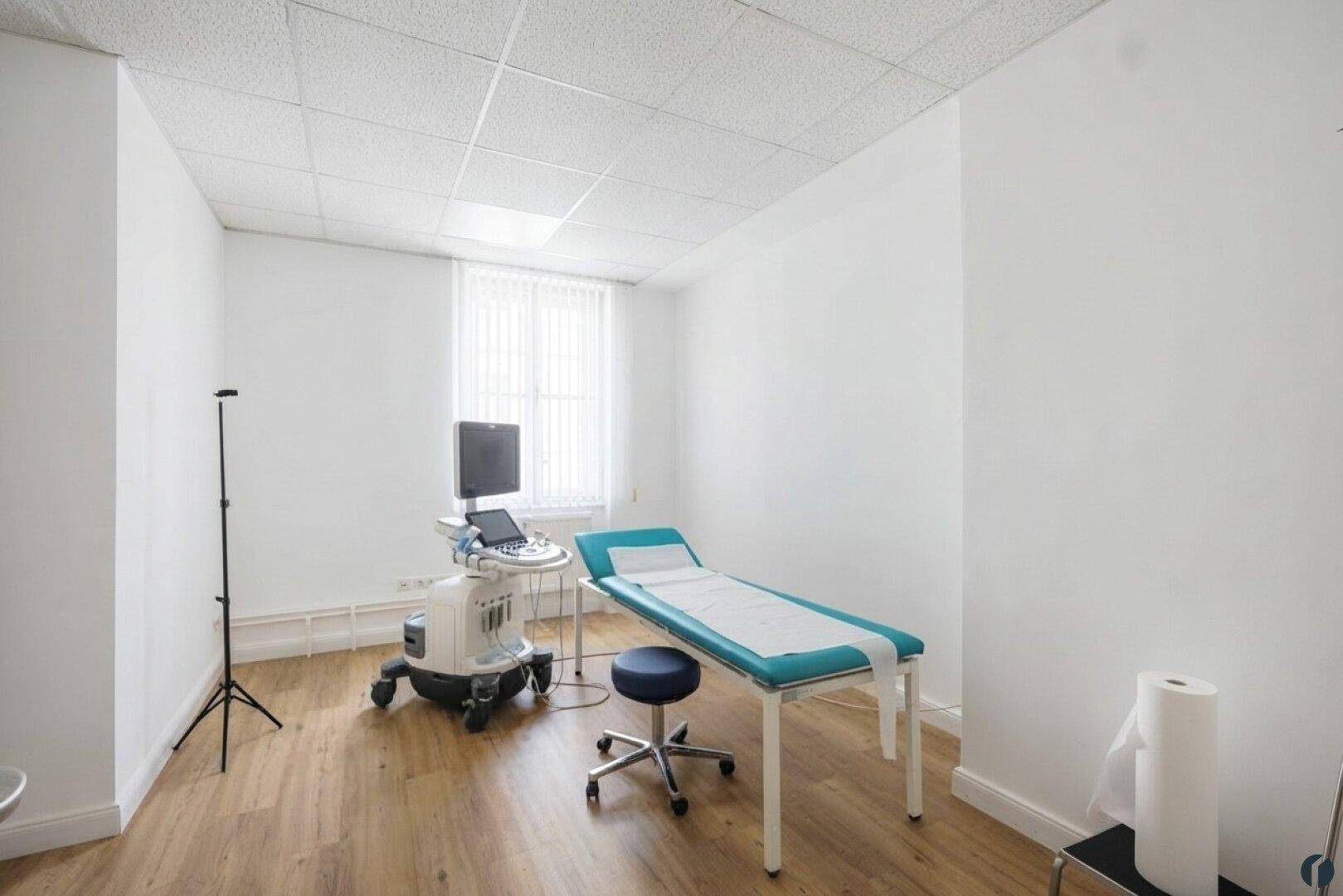 Helles Behandlungszimmer mit Untersuchungsliege und medizinischer Ausrüstung, ideal für Arztpraxen.