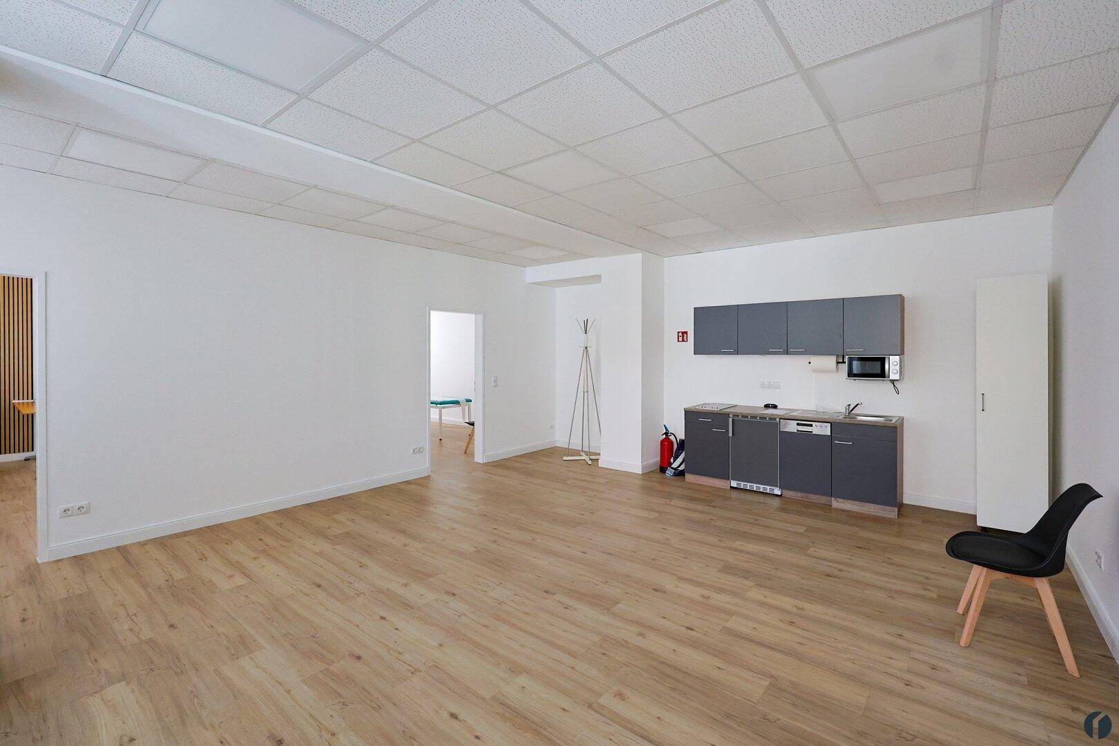 Geräumiger, leerer Büroraum mit integrierter Küchenzeile und hellem Laminatboden.