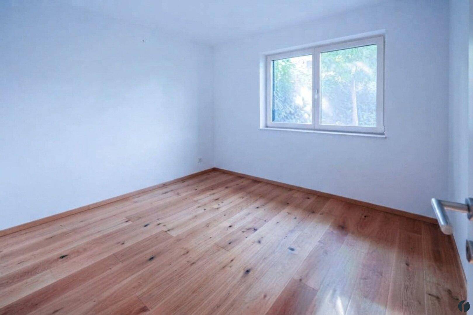 Helles Zimmer mit weißen Wänden und hochwertigem Holzfußboden, ideal als Schlaf- oder Arbeitszimmer.