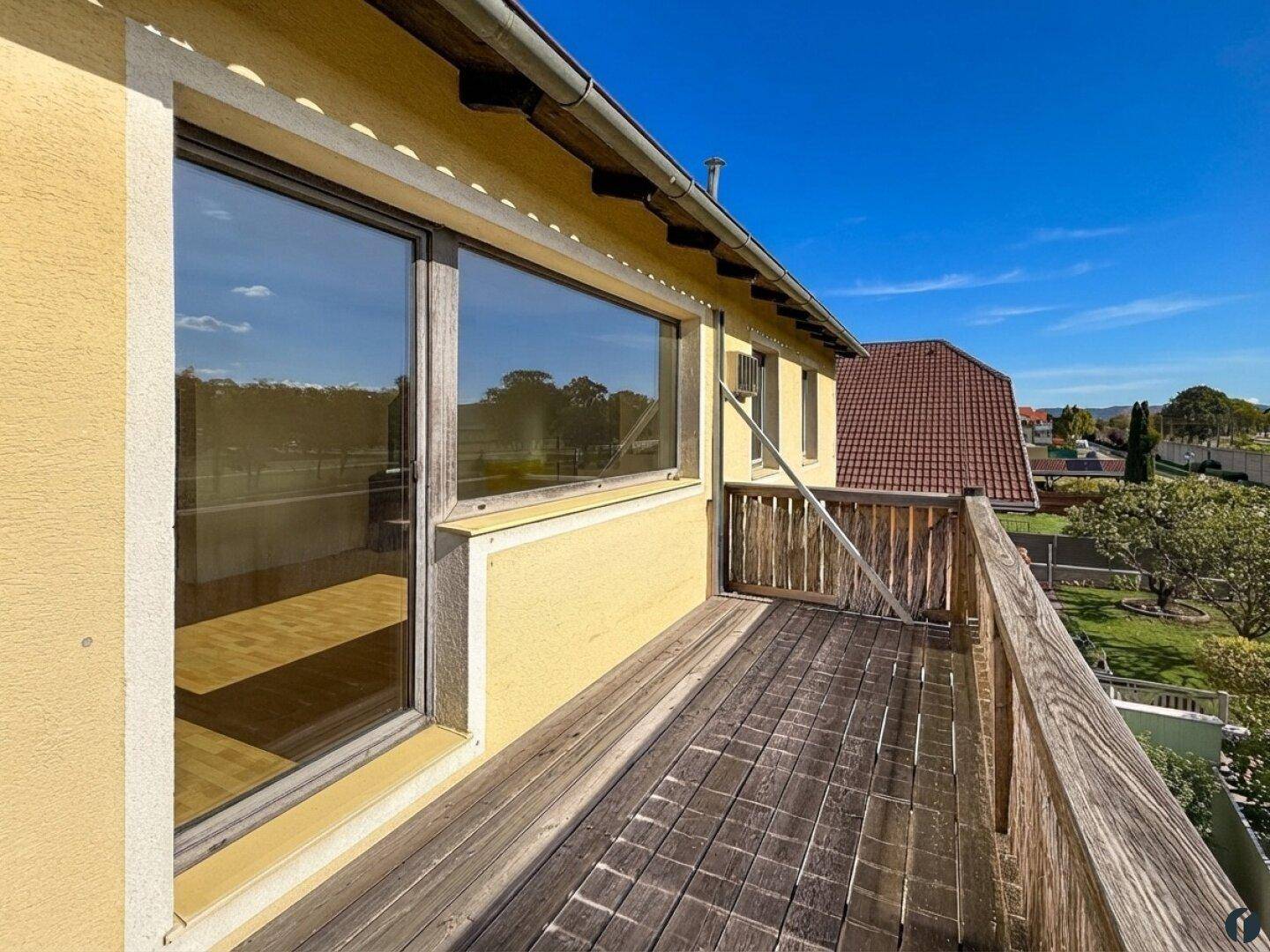 Balkon mit Holzboden und Geländer, bietet einen Blick auf die grüne Umgebung und Dächer.