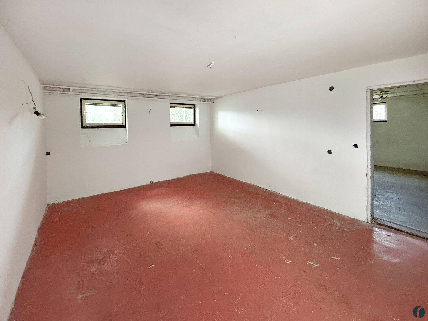 Kellerraum mit rotem Boden, weißen Wänden und kleinen Fenstern, bietet viel Stauraum.