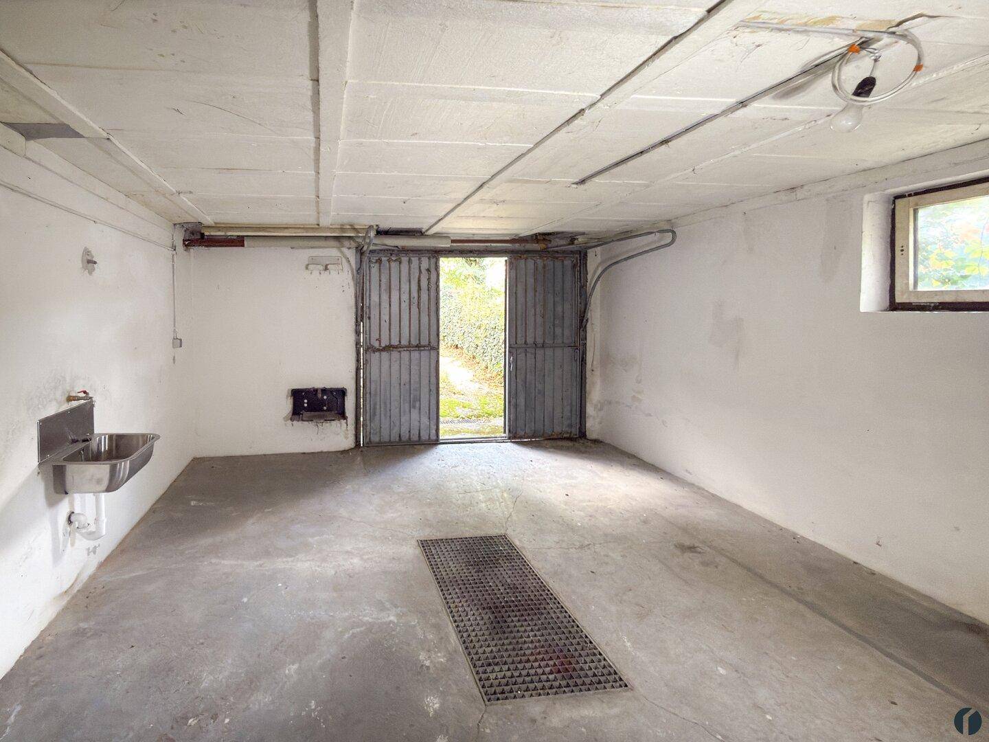 Geräumige Garage mit Betonsockel, Metalltüren und einem Waschbecken, ideal für Fahrzeuge.