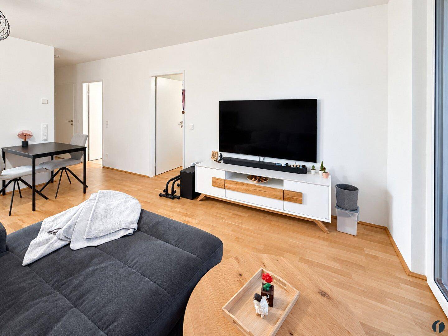 Wohnbereich mit großem Fernseher, modernem Sideboard und hellem Parkettboden, offen gestaltet.