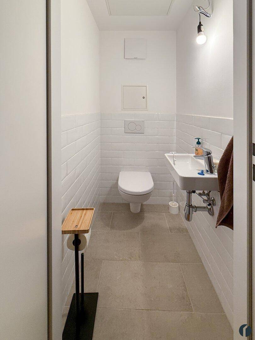 Helles Gäste-WC mit Wand-WC, kleinem Waschbecken und weißen Fliesen, modern gestaltet.