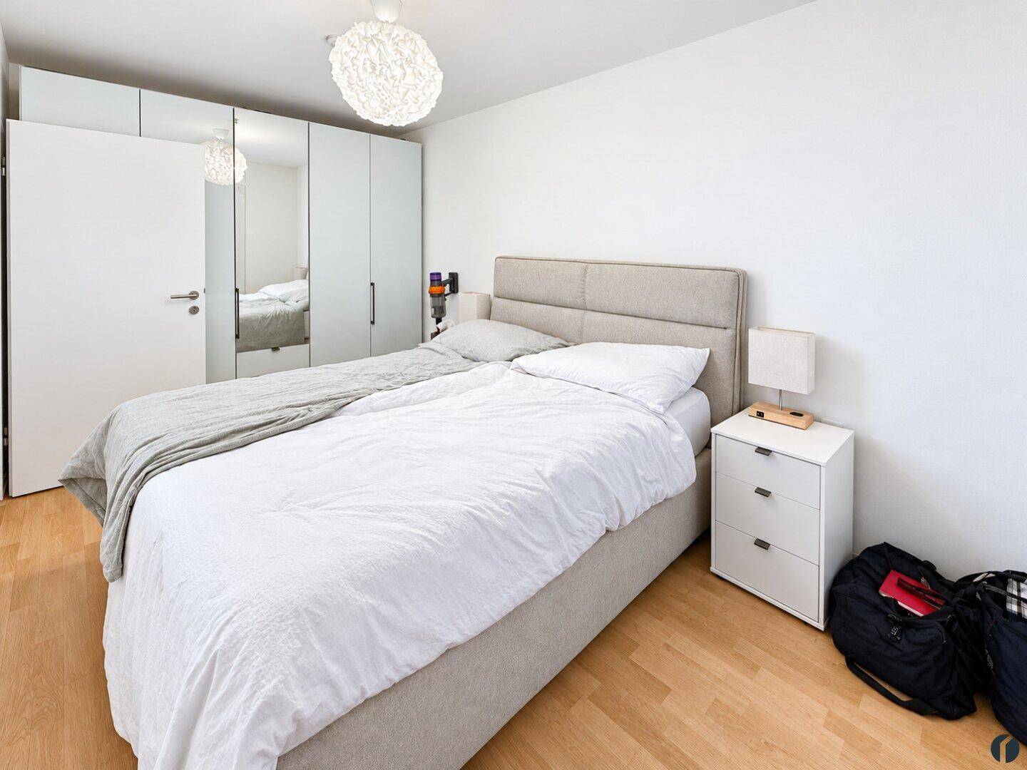 Schlafzimmer mit großem Bett, Spiegelschrank und hellem Ambiente, ausgestattet mit Parkettboden.