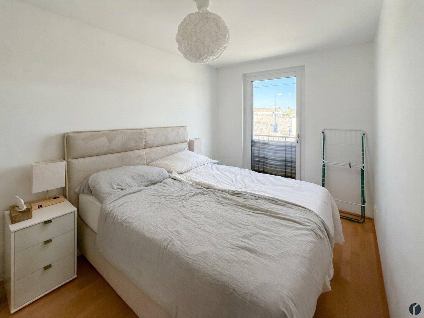 Helles Schlafzimmer mit Zugang zum Balkon und schlichtem, modernem Design und Parkettboden.