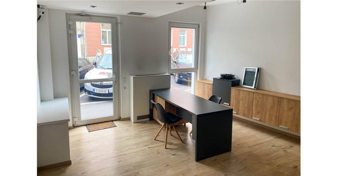 Heller Büroraum mit Holzboden, modernem Schreibtisch und Zugang zur Straße.