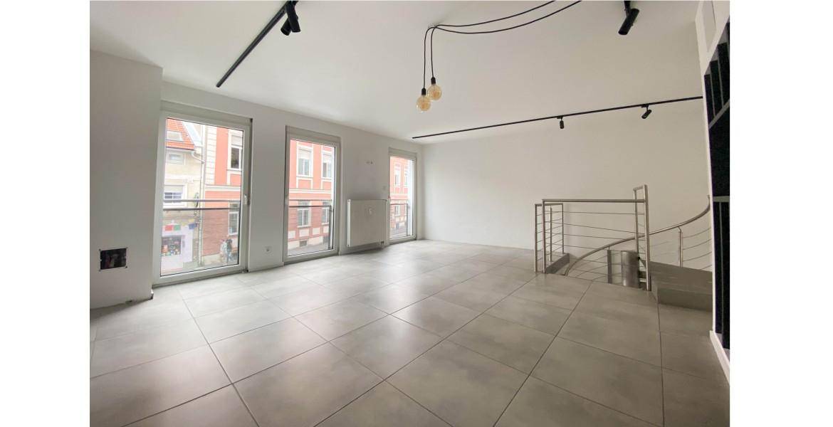 Geräumiger, heller Innenraum mit modernen Fliesen, großen Fenstern mit Blick auf die Straße und einer Wendeltreppe.