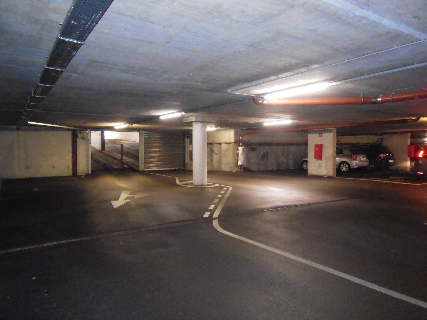 Einfahrt und Ausfahrt der Tiefgarage mit Rolltor, Betonwänden und Pfeilmarkierungen auf dem Boden.