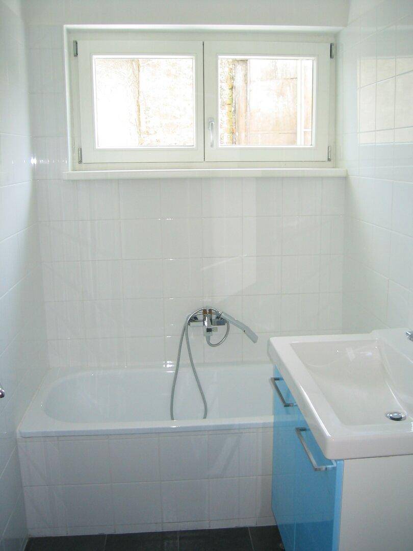 Helles Badezimmer mit Badewanne, Waschbecken und Fenster, in einem gut gepflegten Zustand.