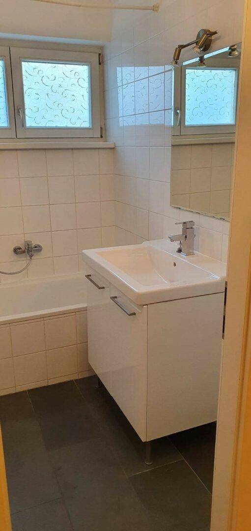 Modernes Badezimmer mit Badewanne, Waschbecken und Fenster für natürliche Belüftung und Licht.