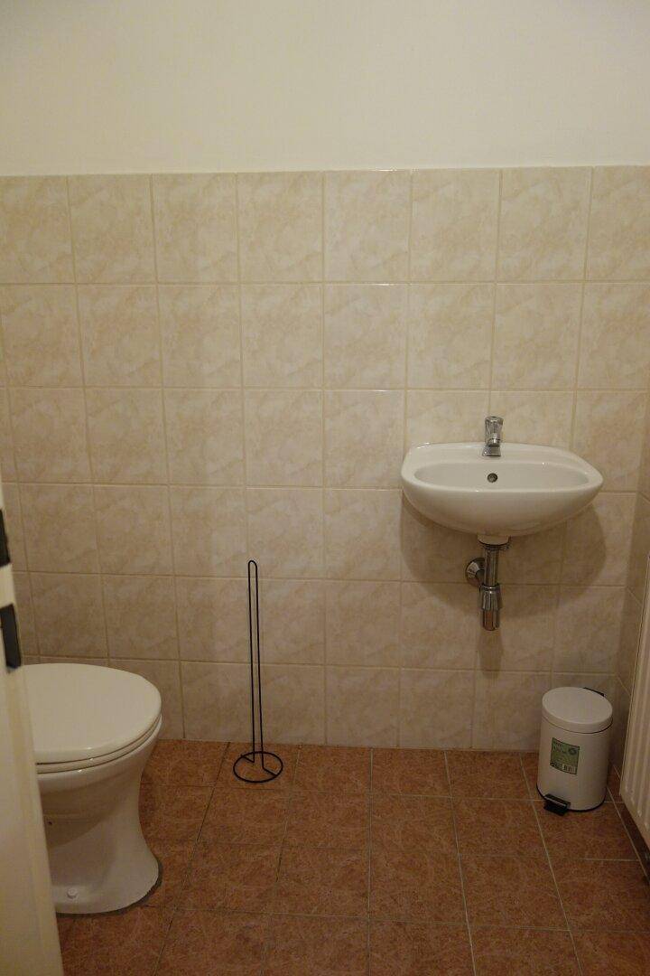 Separates WC mit Toilette und kleinem Handwaschbecken, gefliest in neutralen Farbtönen.