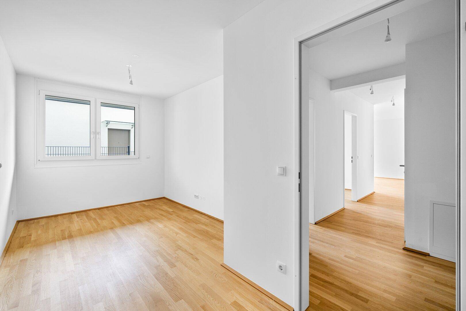 Helles, leeres Zimmer mit Parkettboden und großem Fenster, ideal als Schlafzimmer oder Büro.