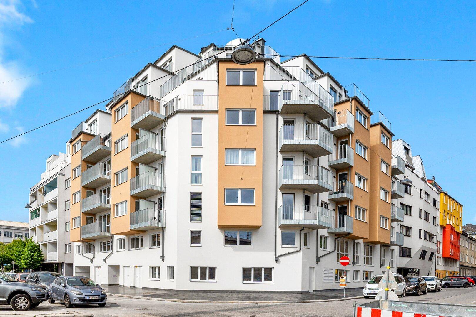 Moderne Wohnhausfassade mit vielen Balkonen und großen Fenstern in städtischer Umgebung.