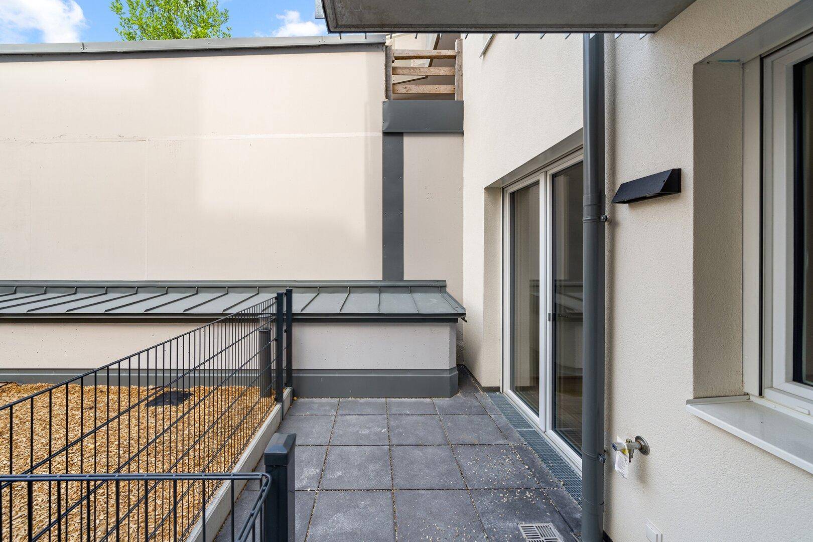 Kleine gepflasterte Terrasse mit Kiesfläche und Zugang zum Gebäude, umgeben von Mauern.