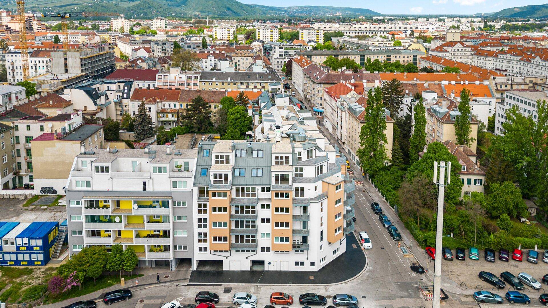 Luftaufnahme eines modernen Wohngebäudes in städtischer Umgebung mit vielfältiger Architektur und vielen Fenstern.