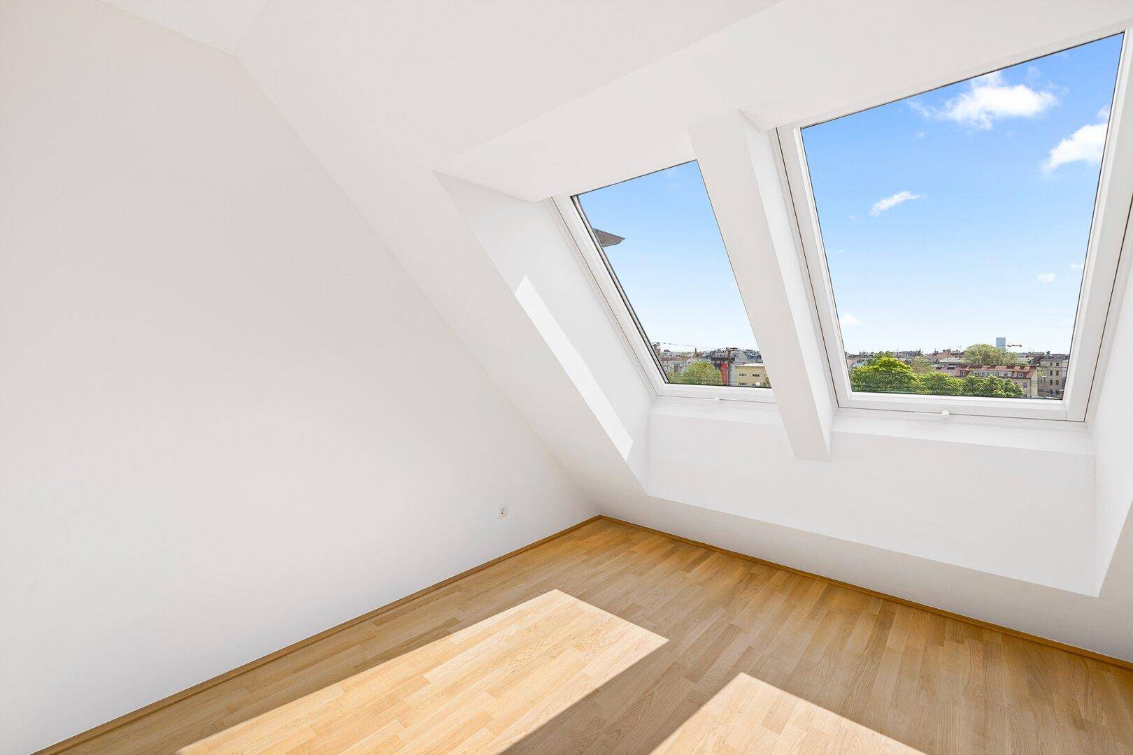 Helles Zimmer im Dachgeschoss mit schrägen Wänden und zwei großen Dachfenstern für viel Licht.