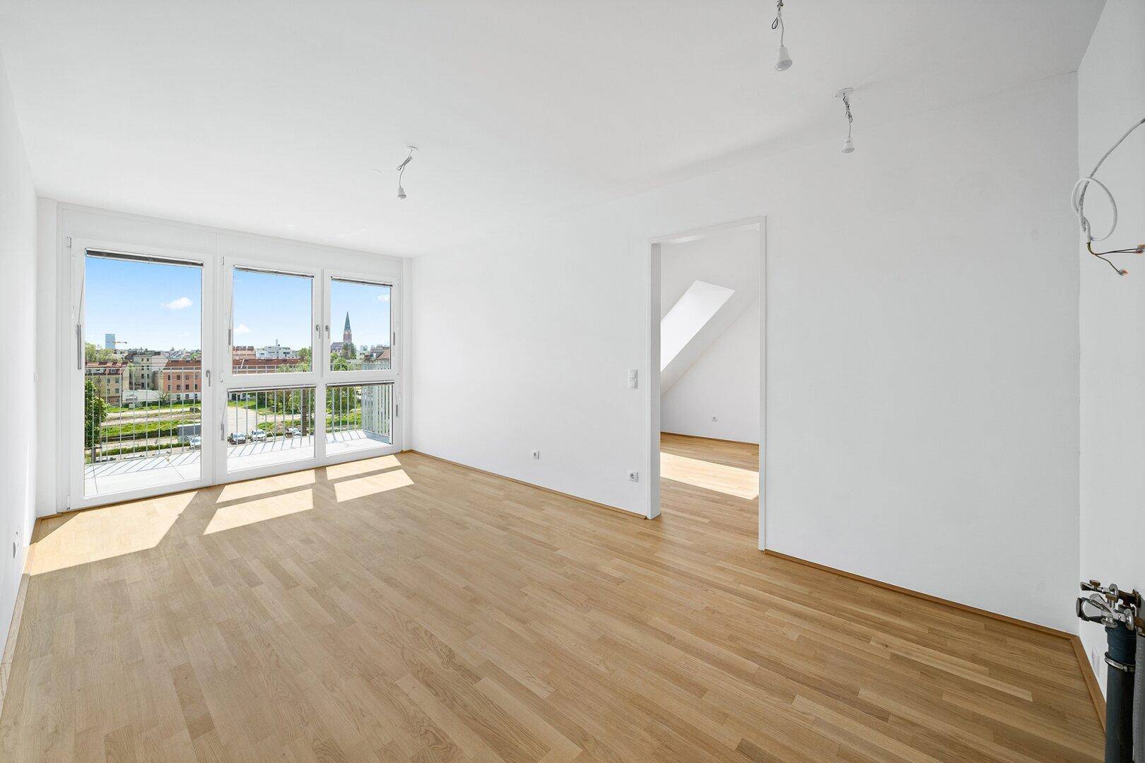 Lichtdurchfluteter Wohnbereich mit Holzboden und Balkonzugang, angrenzend an ein Zimmer im Dachgeschoss.