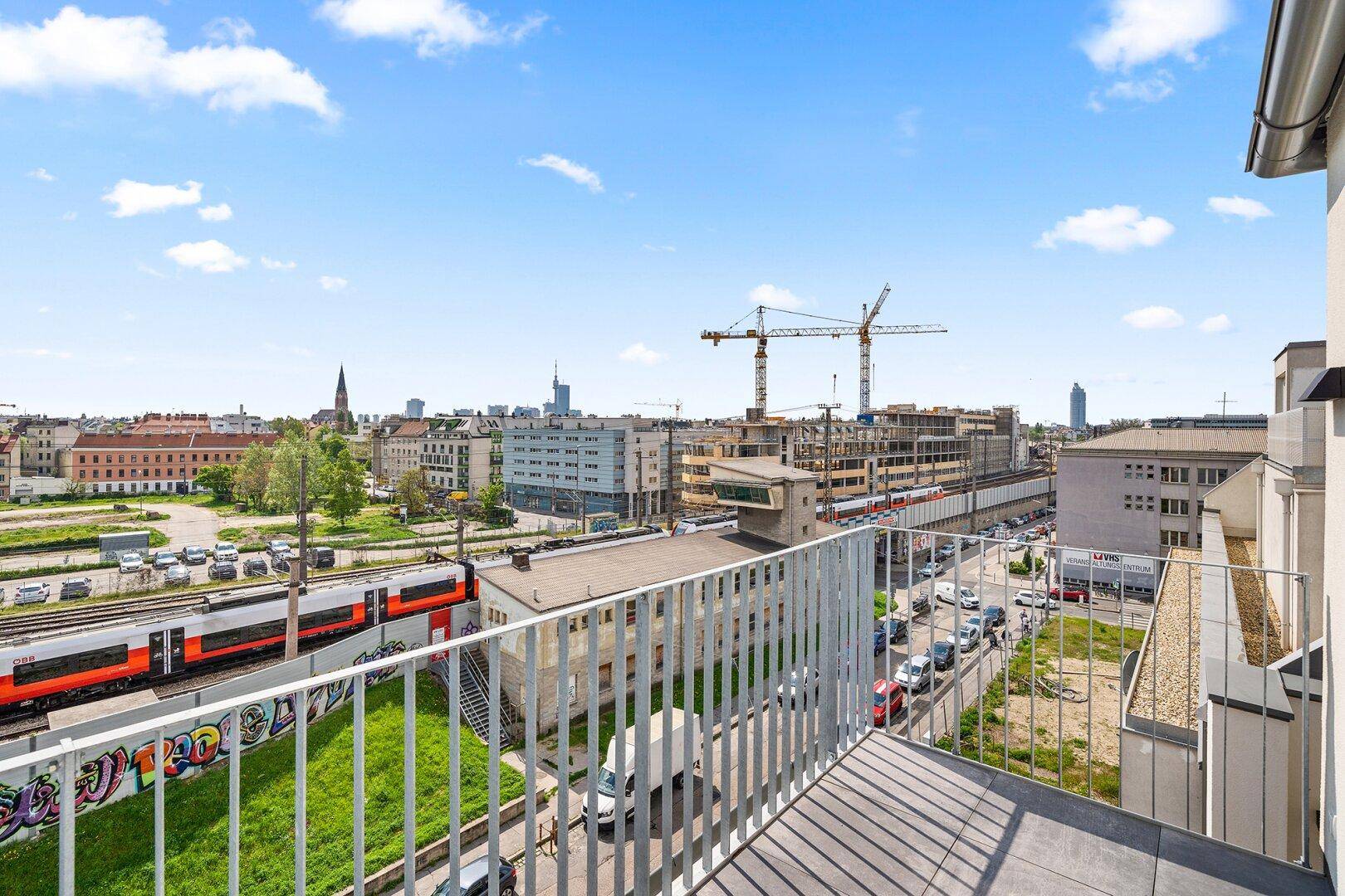 Balkon mit weitem Blick über die Stadt, Bahngleise und umliegende Gebäude unter blauem Himmel.