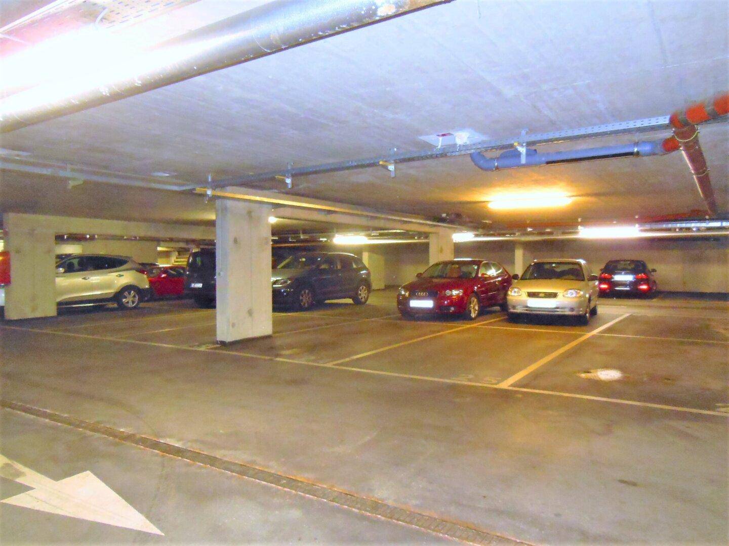 Weitere Ansicht der Tiefgarage mit geparkten Fahrzeugen und klar markierten Stellplätzen.