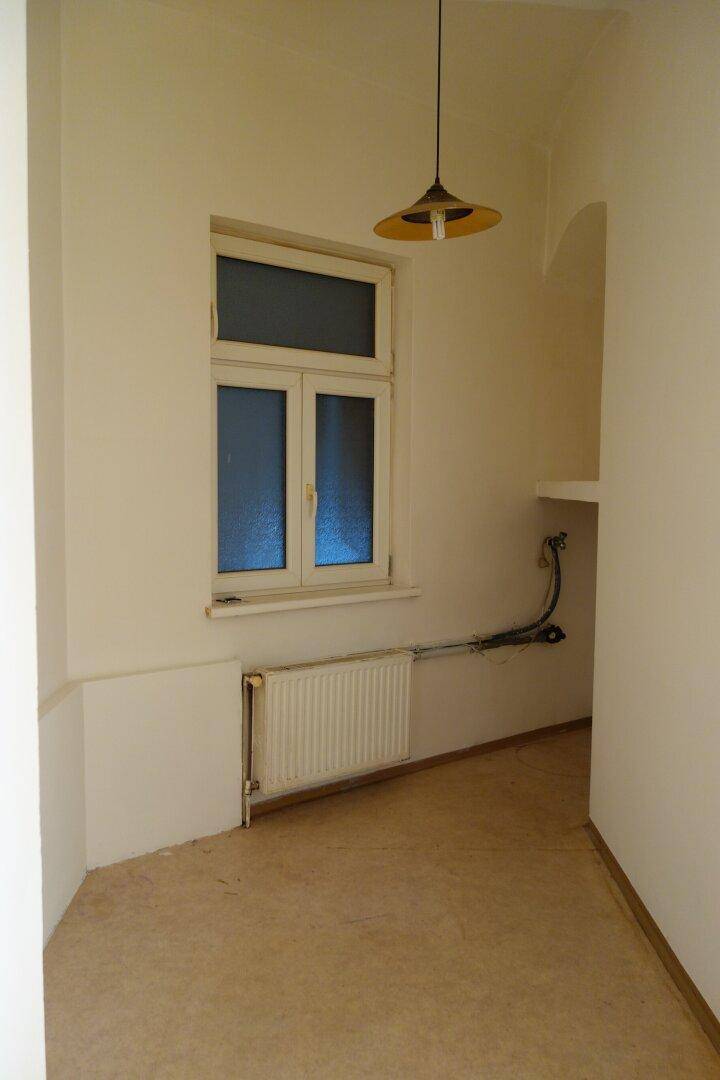 Leerer Küchenbereich mit Fenster, Heizkörper und Anschlüssen für eine zukünftige Küchenzeile.