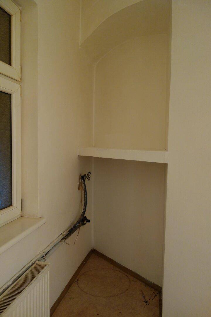 Nische im Küchenbereich mit Anschlüssen und Regal, ideal für zusätzlichen Stauraum.