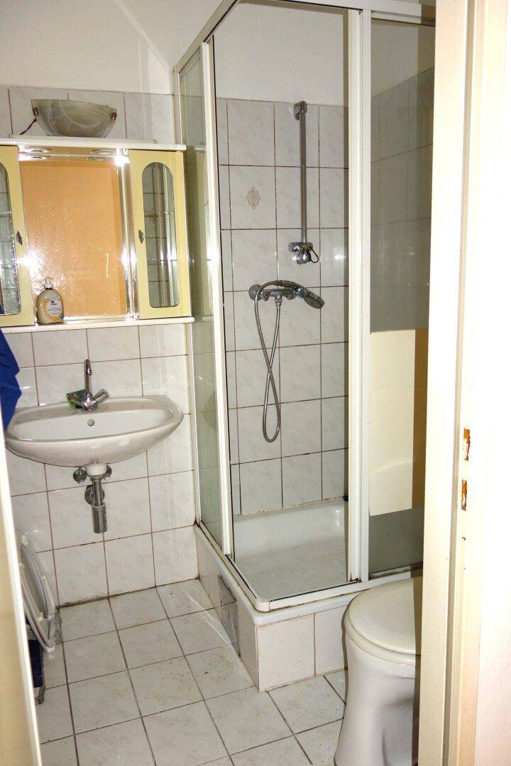 Kleines Badezimmer mit Duschkabine, Waschbecken und Toilette, gefliest in Weiß und Beige.