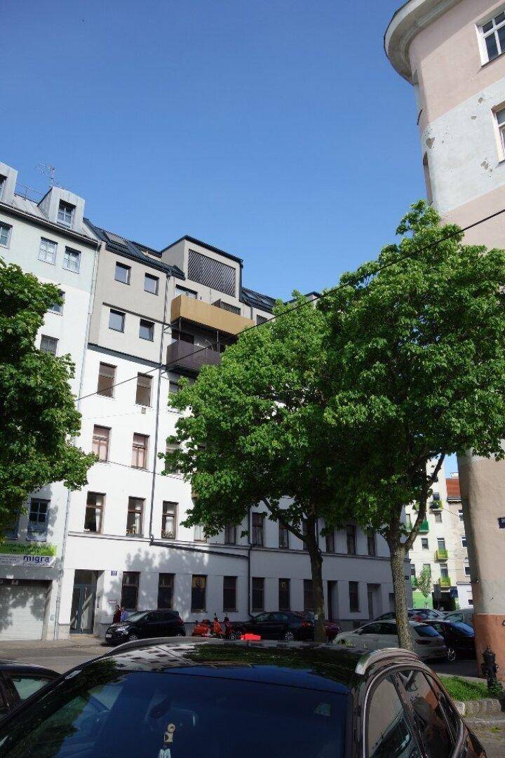 Ansicht eines modernen Wohngebäudes mit Bäumen und parkenden Autos an einem sonnigen Tag.