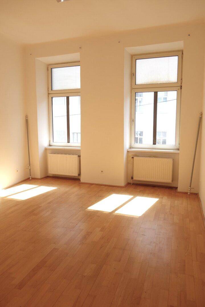 Geräumiges, helles Zimmer mit Holzboden und zwei großen Fenstern, die viel Licht hereinlassen.