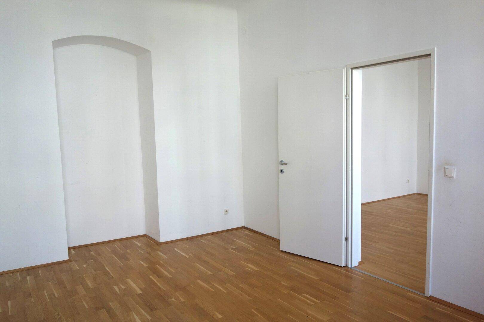Leeres Zimmer mit Parkettboden und einer dekorativen Nische, bietet vielseitige Nutzungsmöglichkeiten.