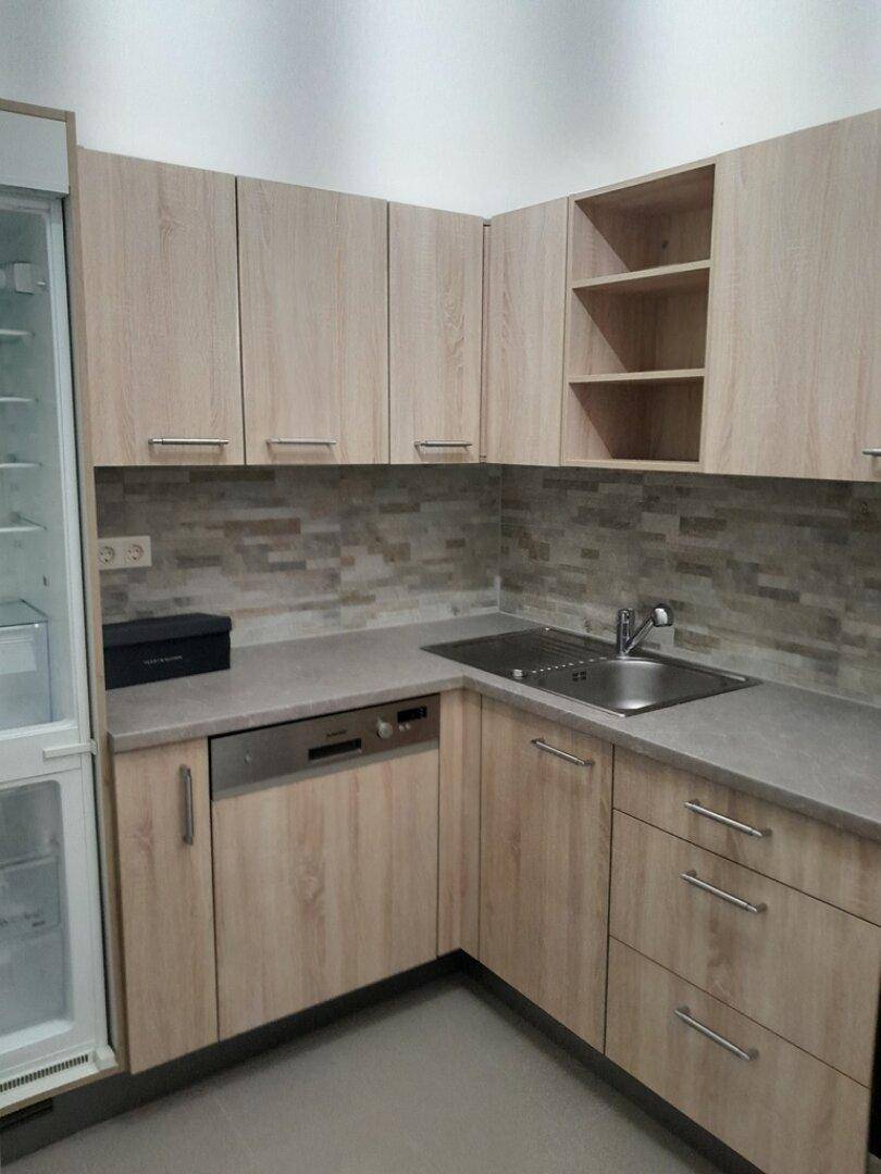 Moderne Einbauküche mit hellen Holzfronten, Spüle und integriertem Geschirrspüler.