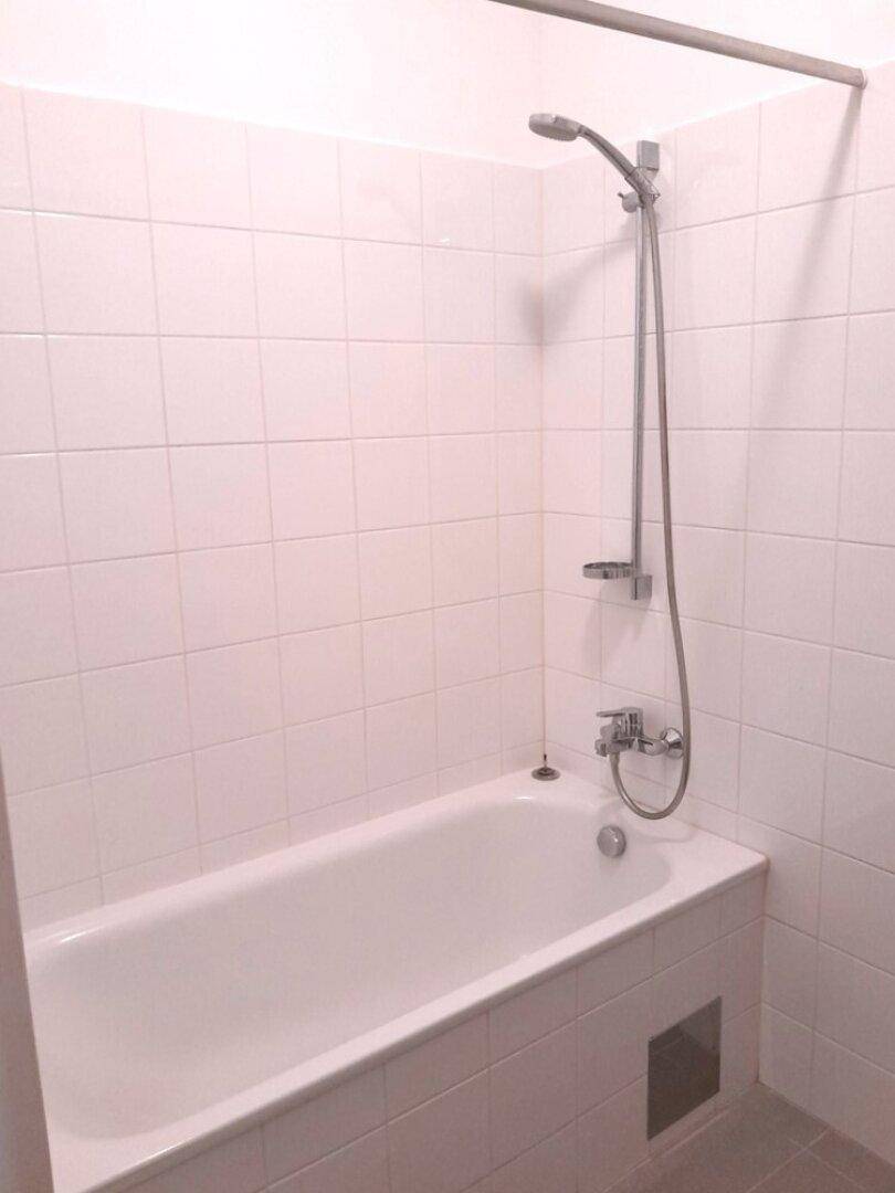 Helles Badezimmer mit weiß gefliester Badewanne und Duschvorrichtung.