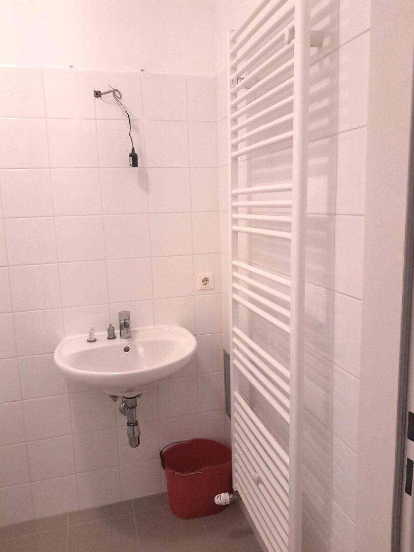 Badezimmer mit Waschbecken, weißen Fliesen und einem praktischen Handtuchheizkörper.