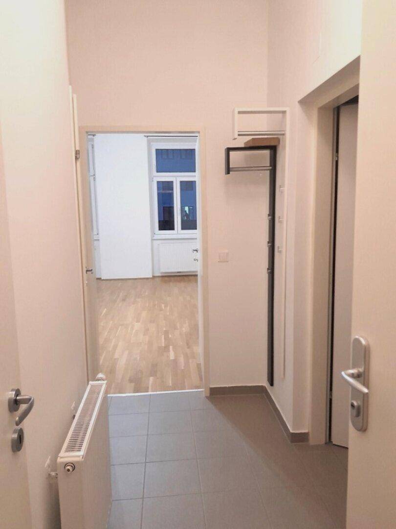 Flur mit Fliesenboden und Garderobenbereich, der den Blick in ein weiteres Zimmer freigibt.