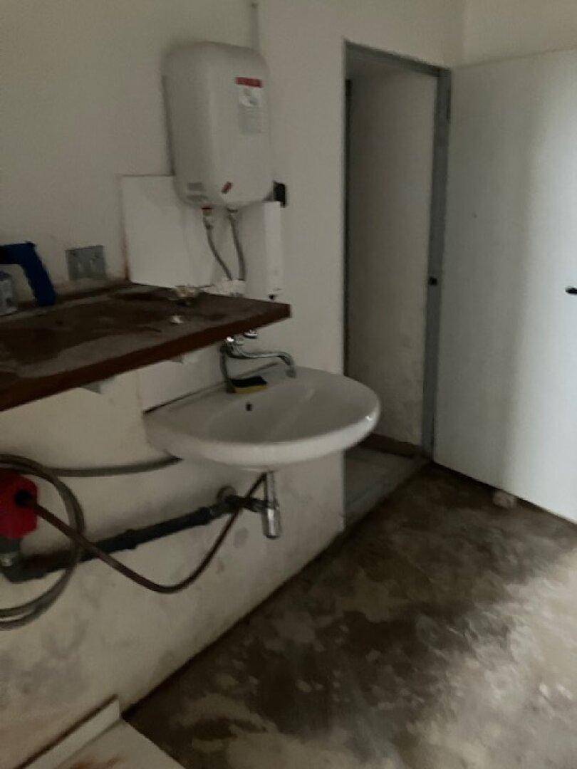 Kleiner Hauswirtschaftsraum mit Waschbecken, Warmwasserbereiter und einer einfachen Holzablage.